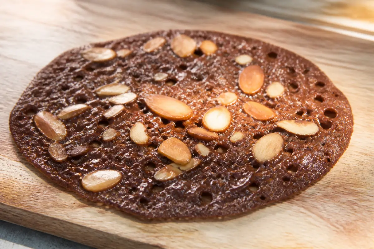 Tuile au chocolat avec amandes sur planche en bois éclairée par le soleil